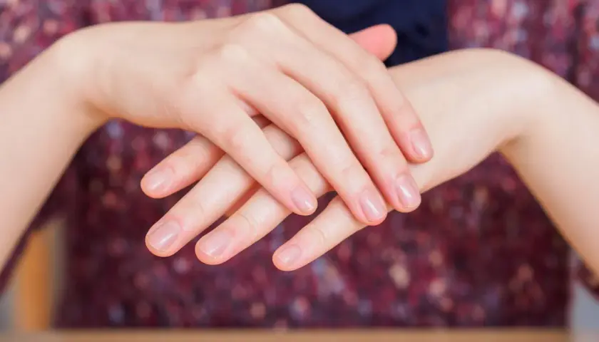 Dłonie z naturalnymi paznokciami, delikatnie skrzyżowane. Choć manicure japoński ma wiele zalet, warto pamiętać o jego potencjalnych wadach.